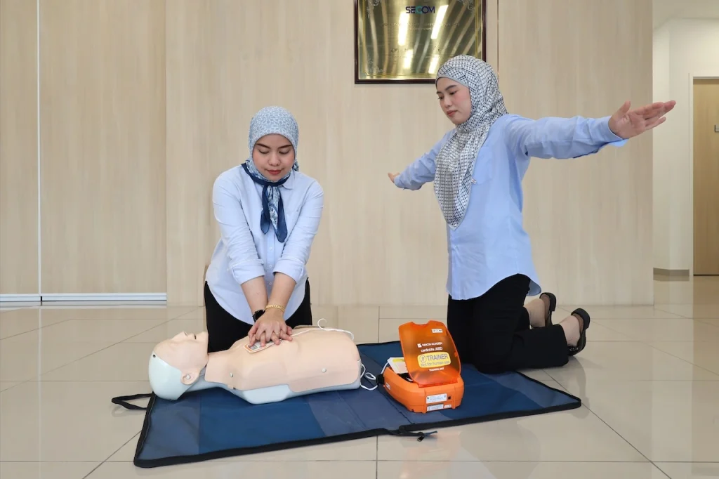 Employees performing CPR and automated external defibrillator training on a manikin during workplace first aid practice