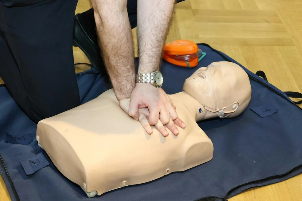 CPR training demonstration on a manikin using an automated external defibrillator during first aid practice.