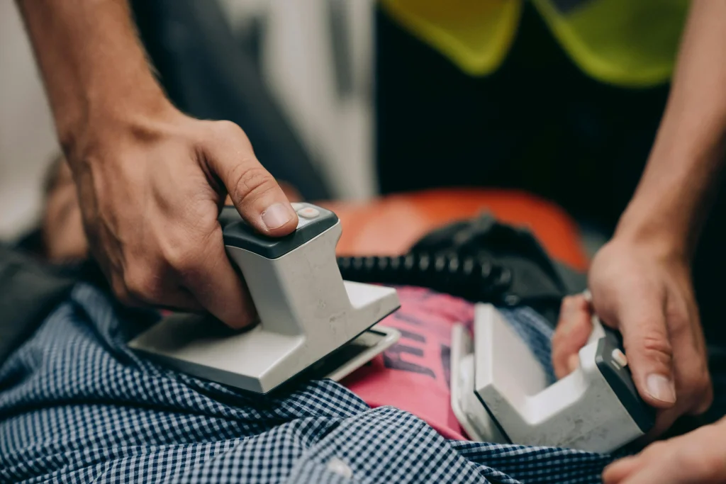 Person using an AED defibrillator during an emergency response to assist a collapsed individual.