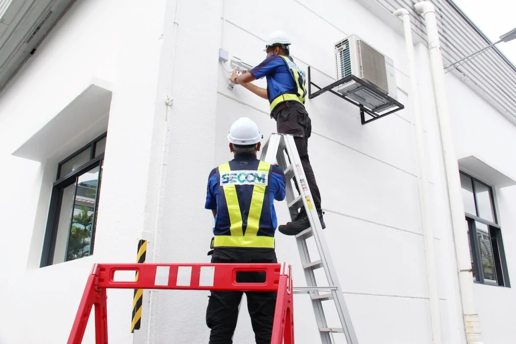 SECOM technicians installing CCTV equipment on the exterior of a commercial building for a security system setup