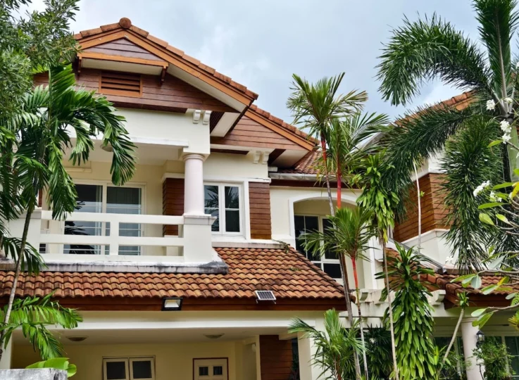 residential-security-solutions-malaysia-landed-house Two-storey landed house in Malaysia with a tiled roof, balcony and tropical palms, fitted with an outdoor security floodlight for residential home security