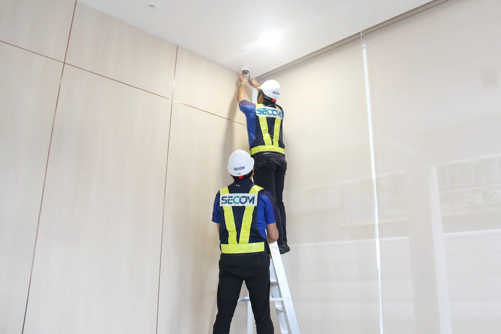 SECOM Malaysia technicians installing a ceiling-mounted security device for a retail alarm system in Malaysia