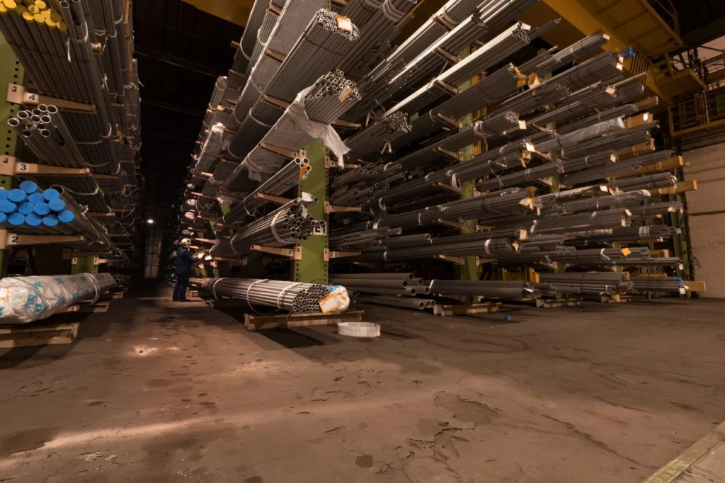 Pipe/rod storage racks, worker checking stock: "Warehouse worker checking stored pipe inventory on industrial racking, reflecting warehouse security best practices"