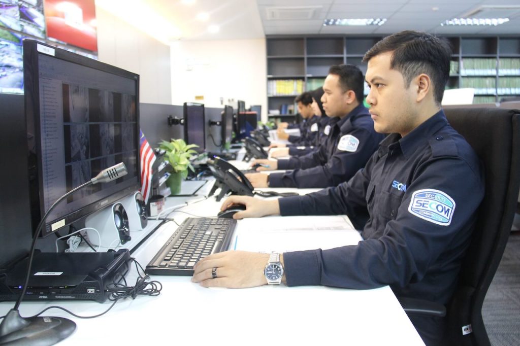 SECOM Malaysia control centre team monitors multiple screens with CCTV surveillance for 24/7 central monitoring system.